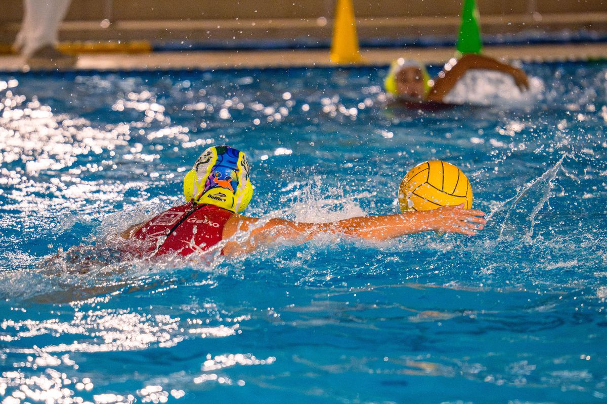 Jugadora de waterpolo nada hacia el balón amarillo durante una acción de juego.